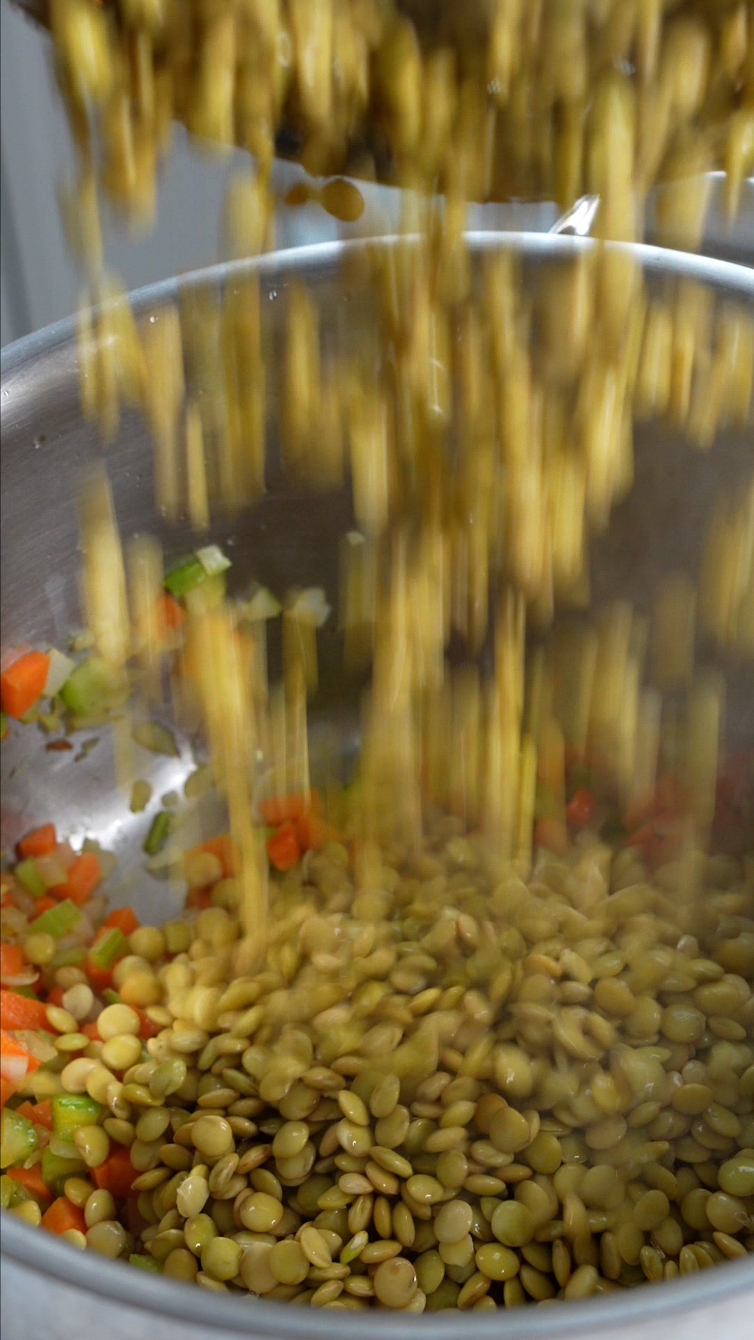 Dry lentils being added to pot with carrot, celery and onions