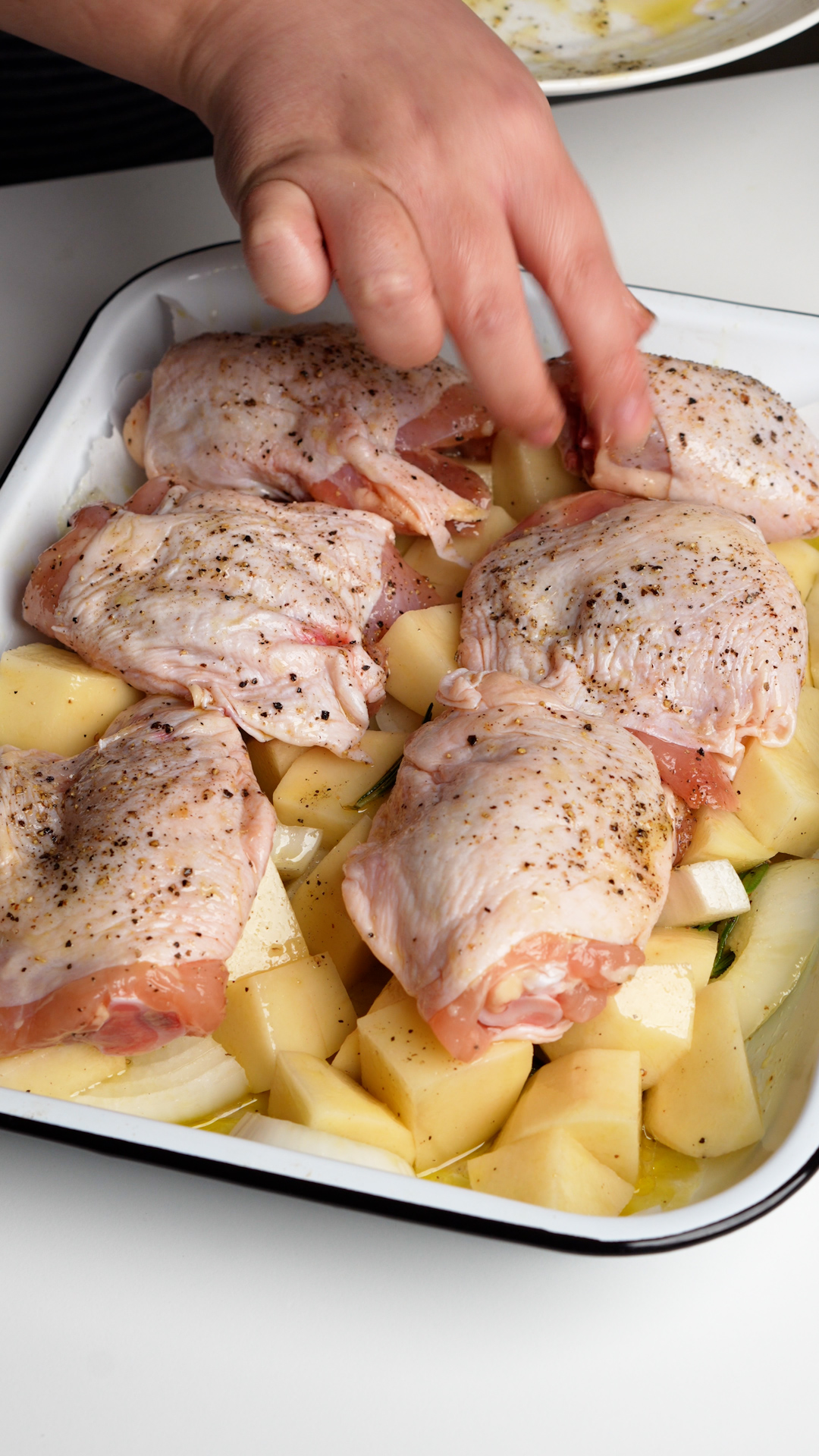 Raw chicken thighs on cut potatoes on a baking dish