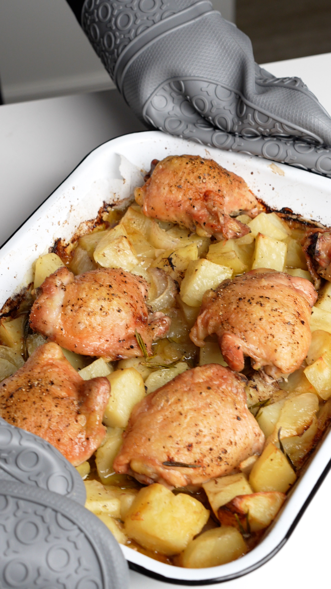 Cooked chicken thighs on a bed of cooked potatoes in a white baking dish