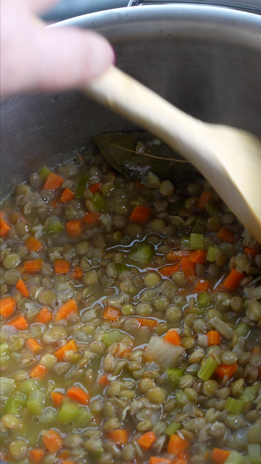 Simmered carrot and lentil soup being stirred with wooden spoon
