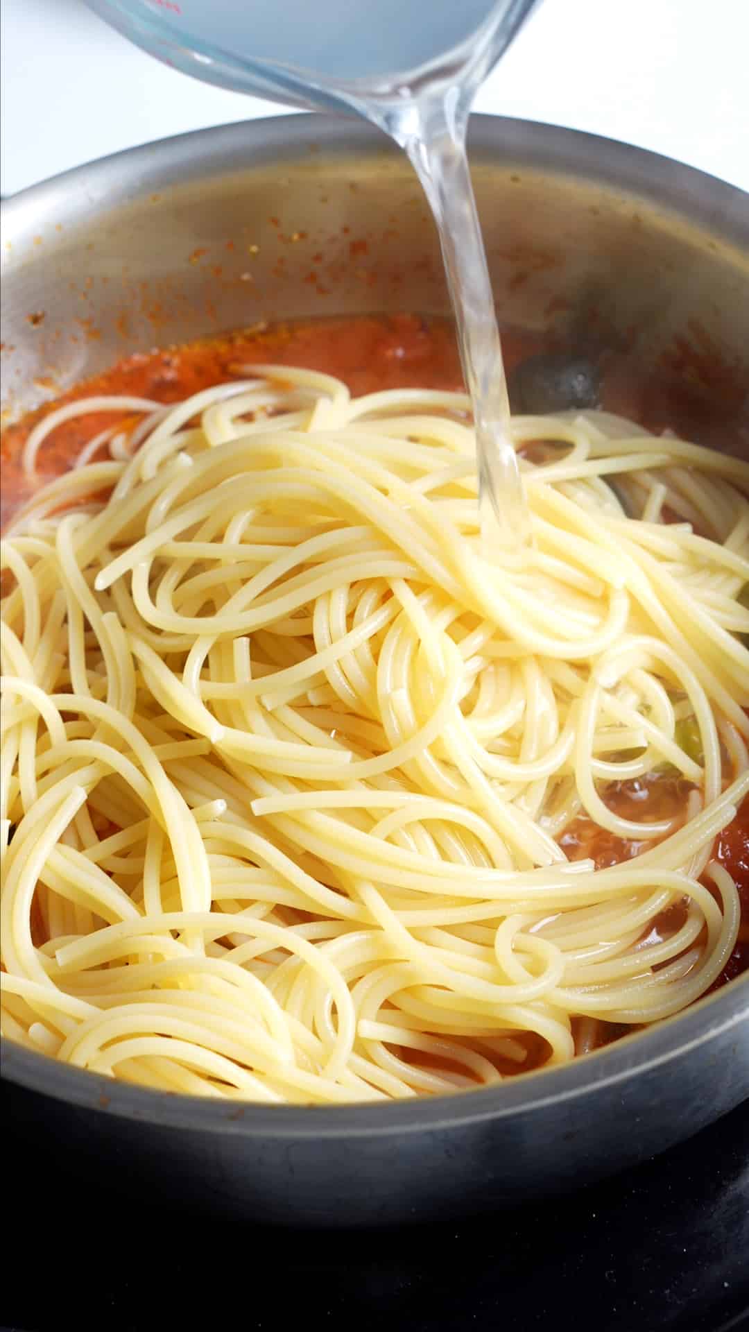 Step by step process on how to make vesuviana pasta - cooked spaghetti in tomato sauce with pasta water being poured in