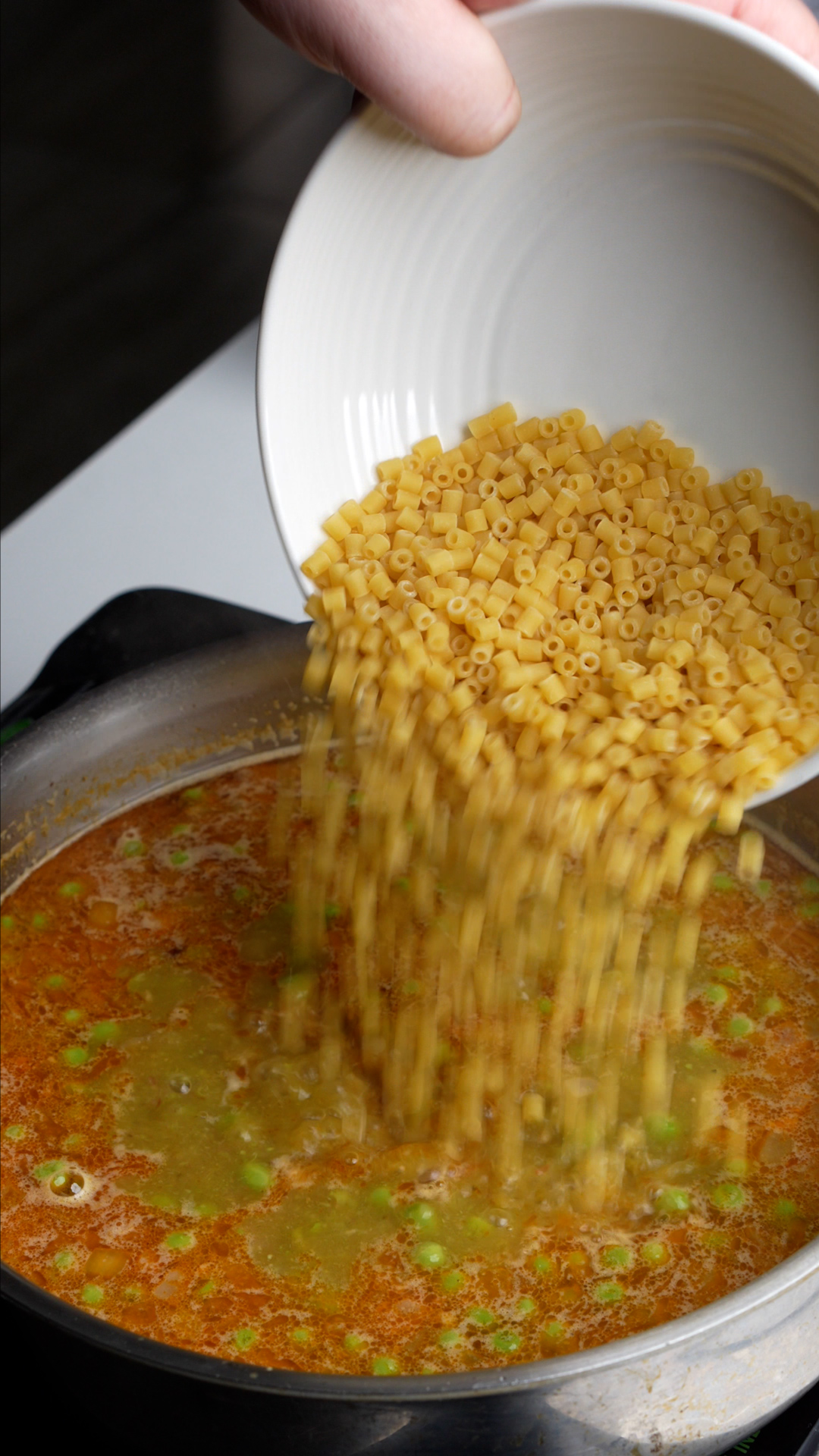 Process photo on how to make pasta e piselli - ditaliani being poured into pasta e piselli mixture