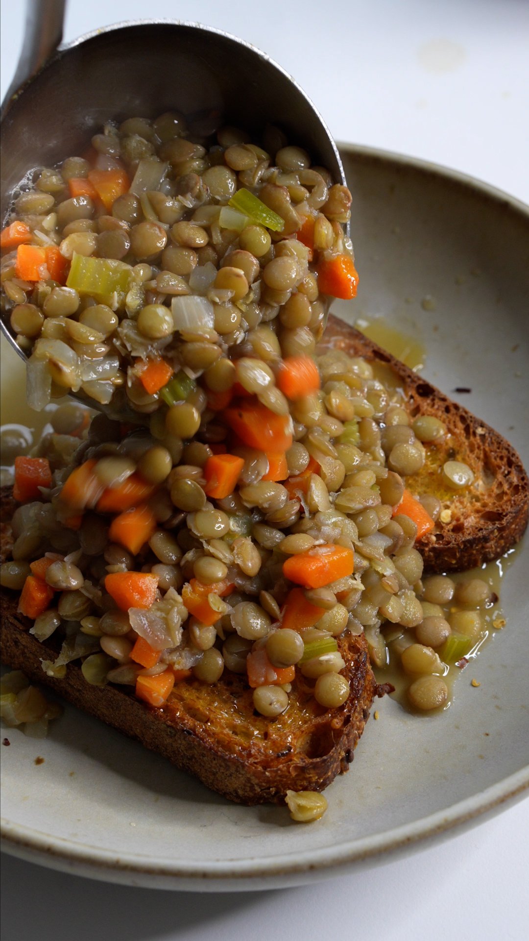 Carrot and lentil soup being ladled onto toasted bread