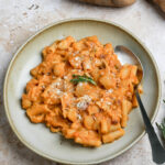 Pasta e patate in a bowl topped with fresh rosemary with russet potatoes in the background