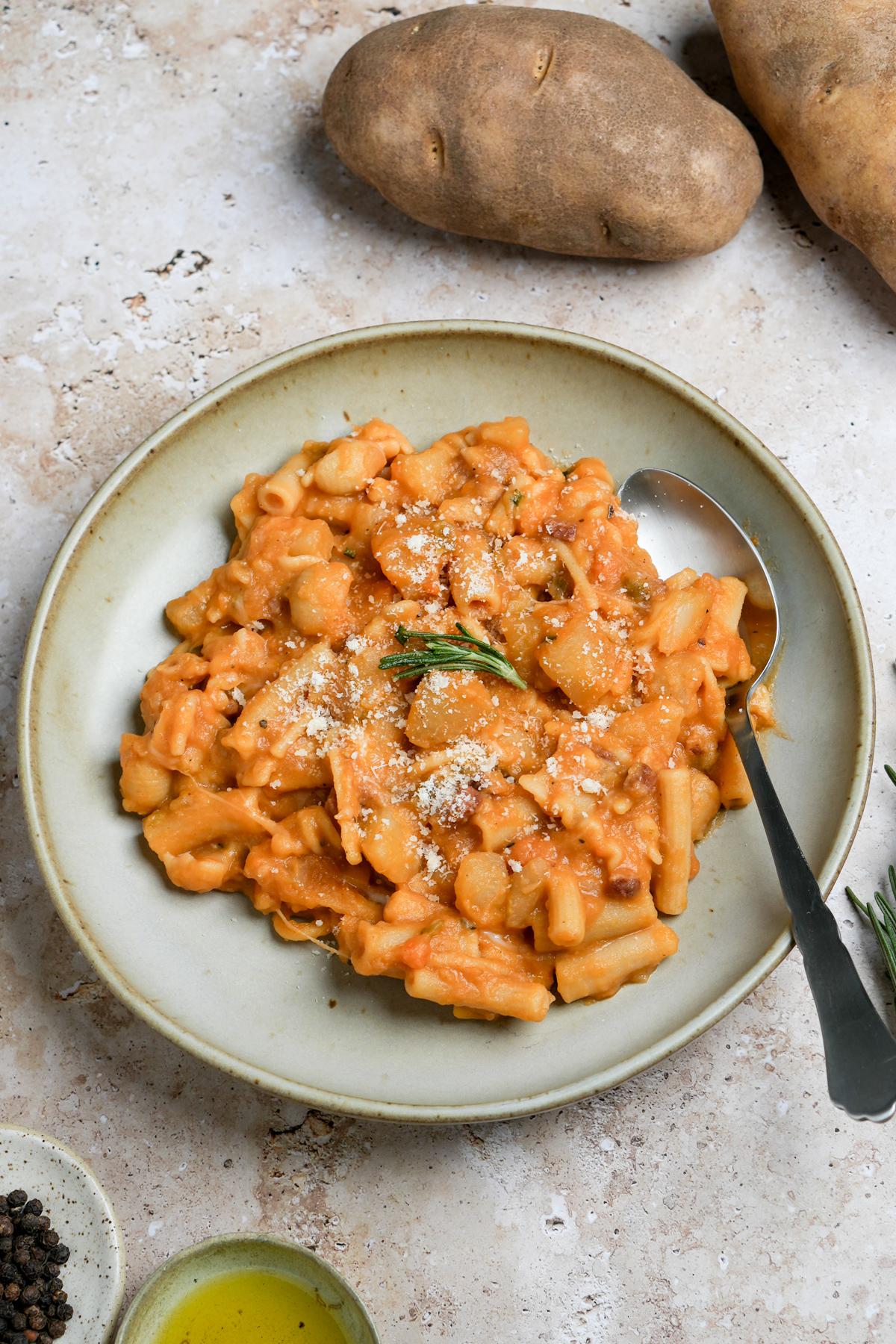 Pasta e patate in a bowl topped with fresh rosemary with russet potatoes in the background