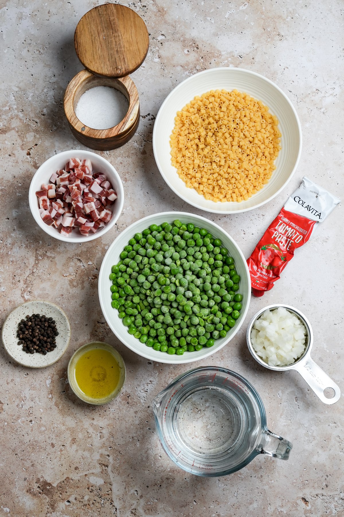 Ingredients for pasta e piselli laid out- small pasta, tomato paste, onion, frozen peas, water, olive oil, pepper, pancetta, salt