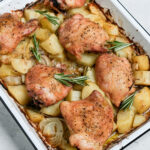 Baked chicken thighs on a baking sheet on a bed of potatoes