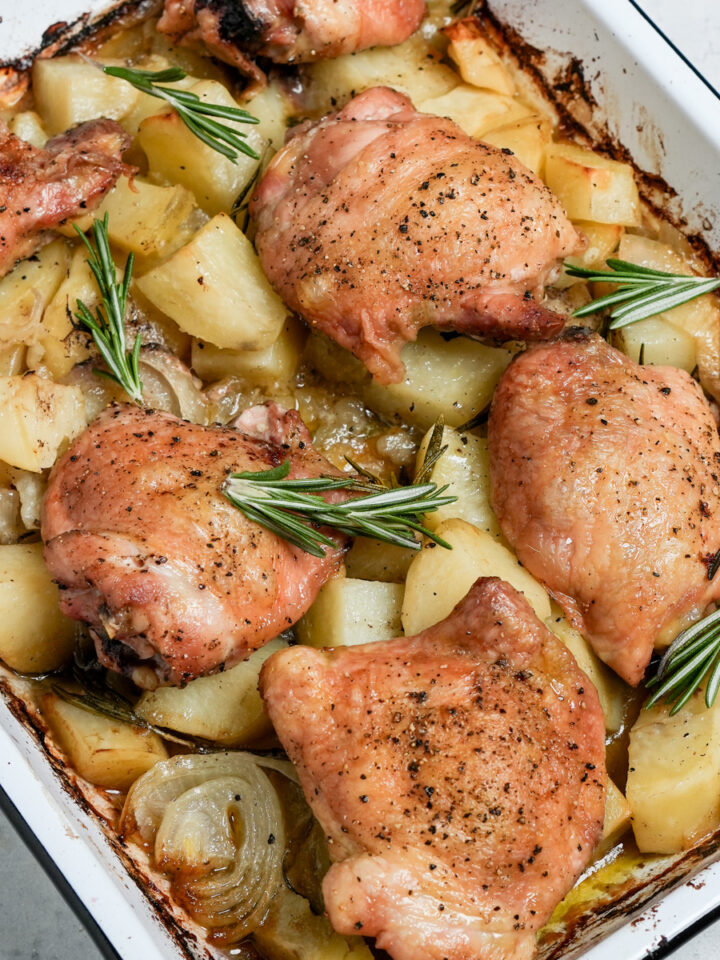Baked chicken thighs on a baking sheet on a bed of potatoes