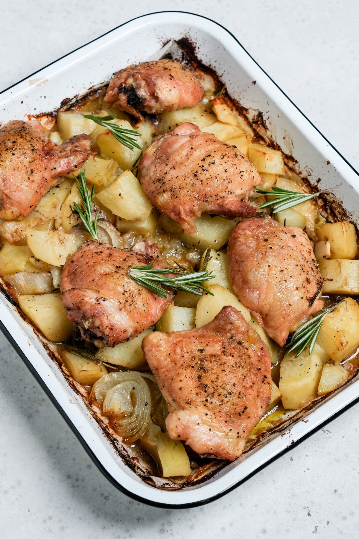 Italian baked chicken in a pan on a bed of potatoes with fresh rosemary sprigs