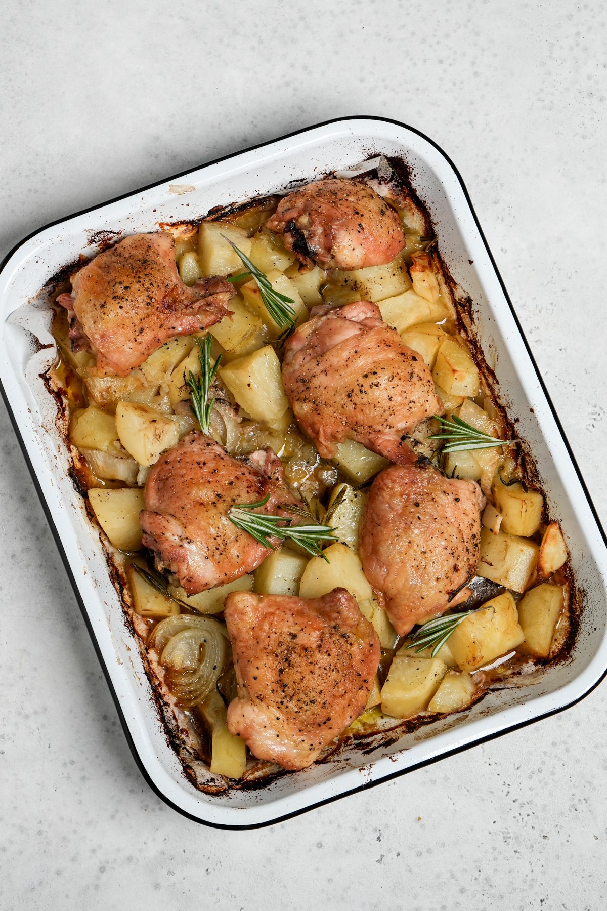 Baked chicken thighs in a baking dish on a bed of cooked potatoes