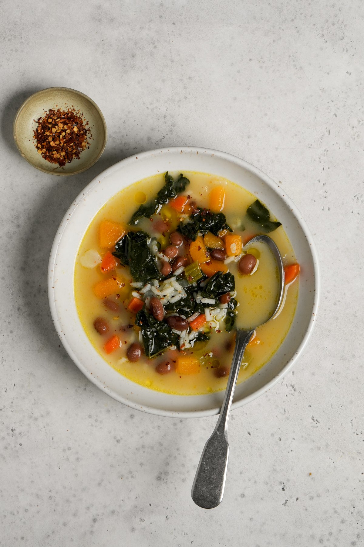 Soup in a bowl with beans, kale, and butternut squash in a bowl with a spoon