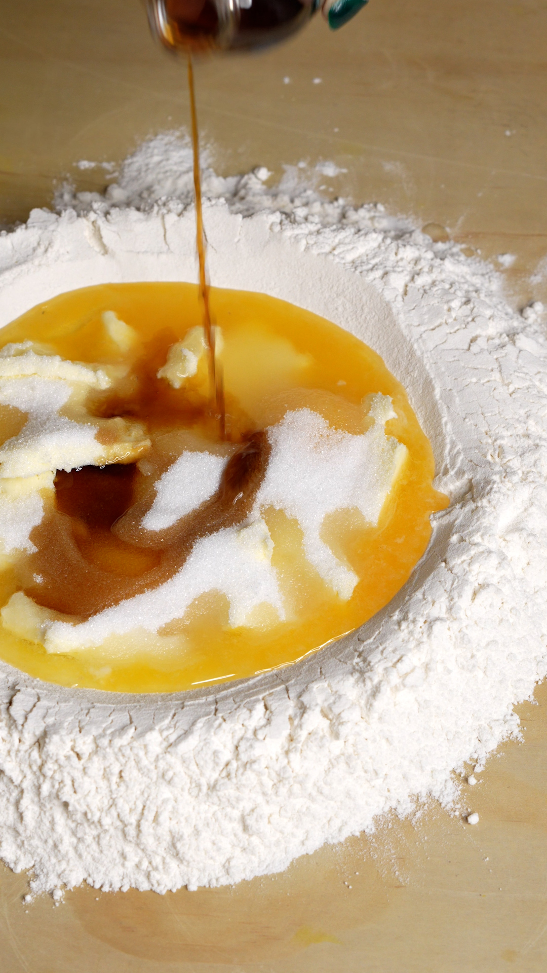 Flour well on a wooden board with eggs, orange juice, sugar, butter and vanilla extract being poured in