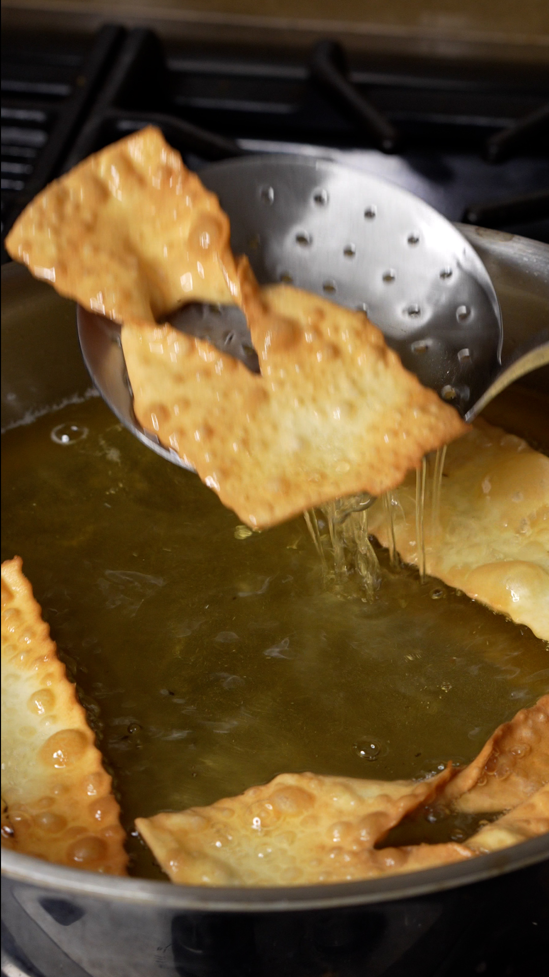 Fried chiacchiere being lifted from hot oil