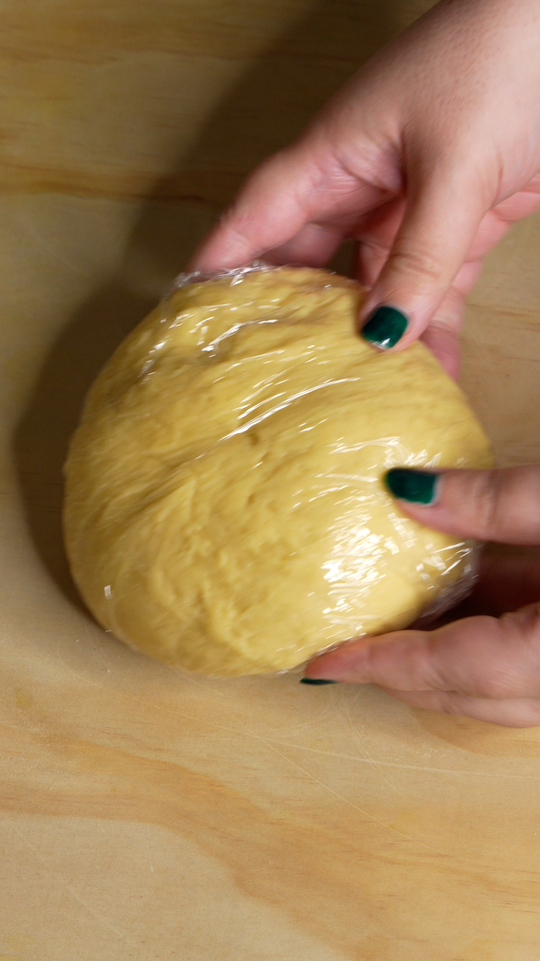 Dough ball wrapped in cling wrap with two hands gripping it