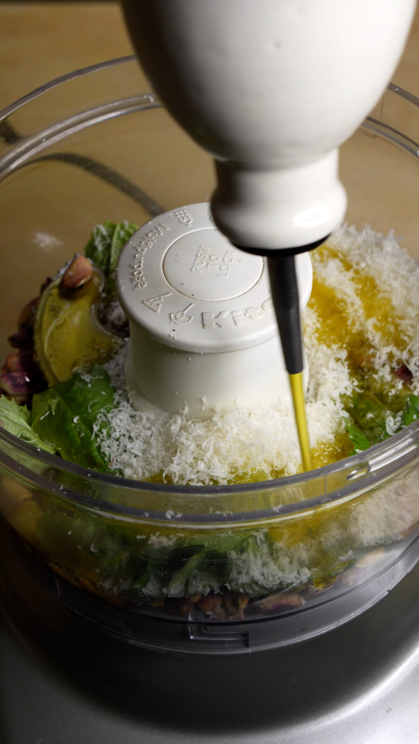 Olive oil being poured into food processor with pistachio pesto ingredients in it
