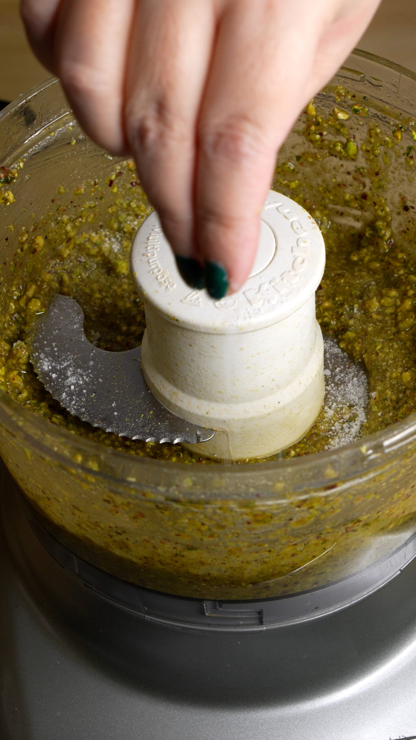 Pinch of salt being added to pistachio pesto in food processor