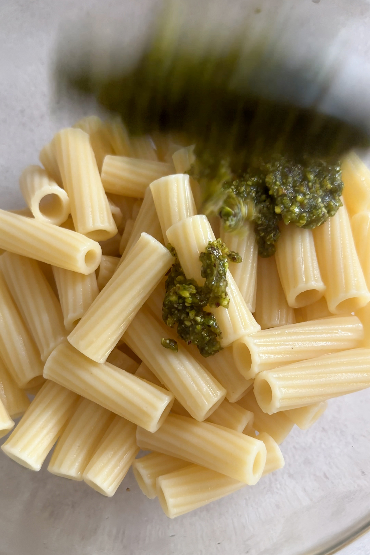 Pistachio pesto being spooned into a bowl with pasta in it