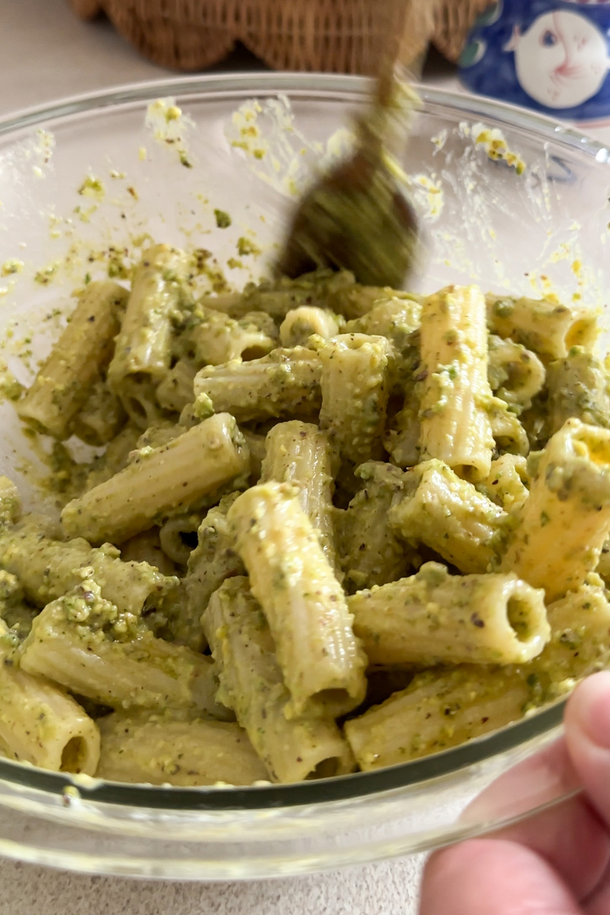 Wooden spoon mixing pasta and pistachio pesto in a bowl