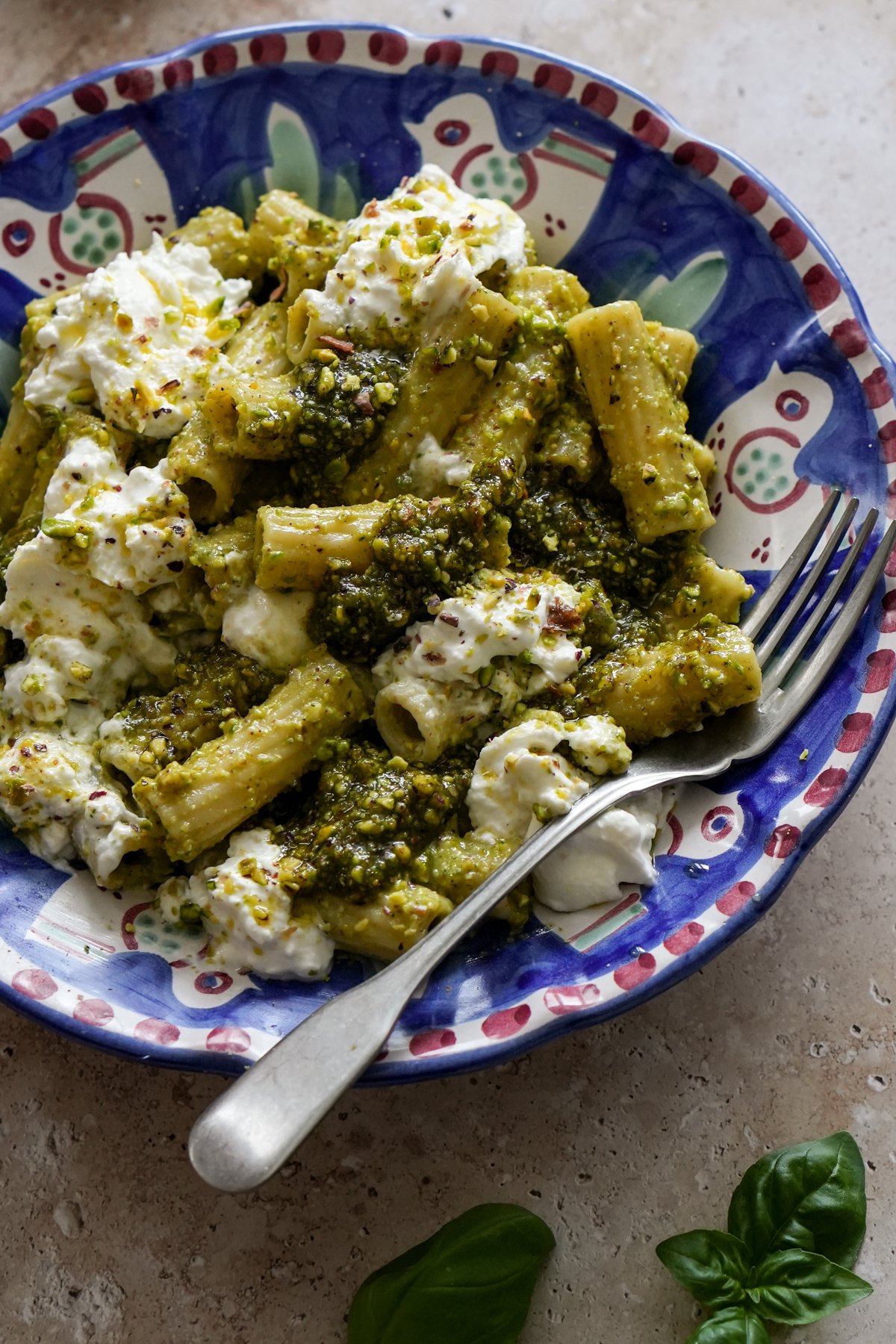Italian pistachio pasta in a plate with a fork, and a few basil leaves to the side