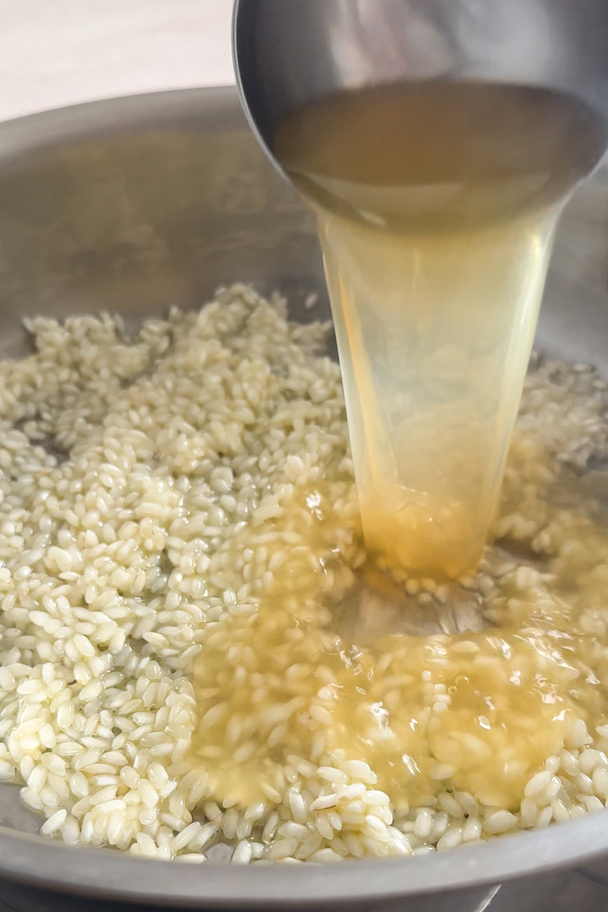 Ladle pouring vegetable broth into pan with arborio rice