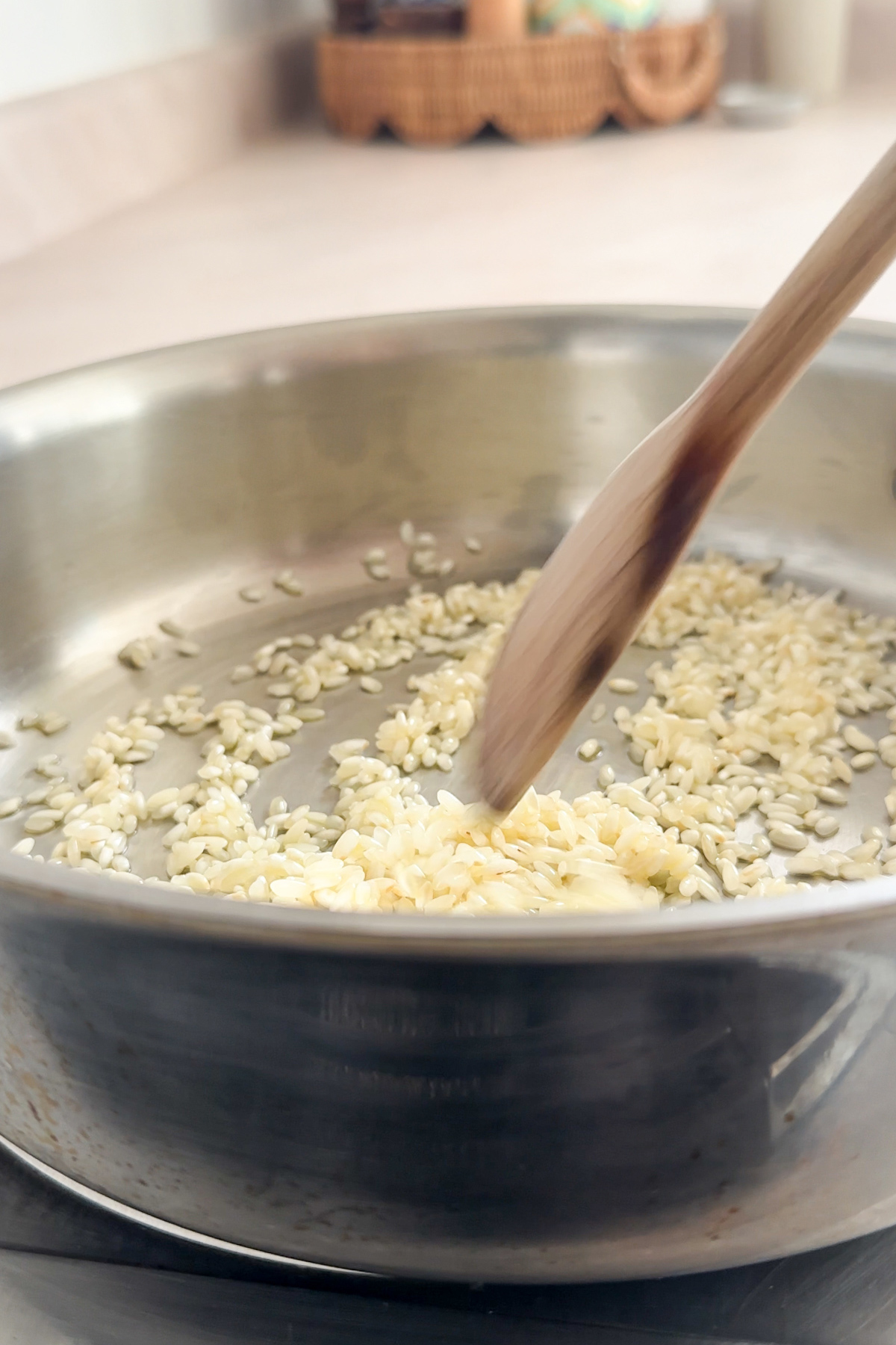 Arborio rice being sauteed in a pan and a wooden spoon stirring it