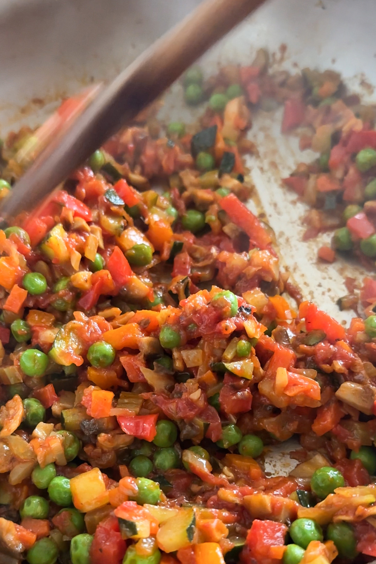 Mixed vegetables being stirred in a pan with a wooden spoon