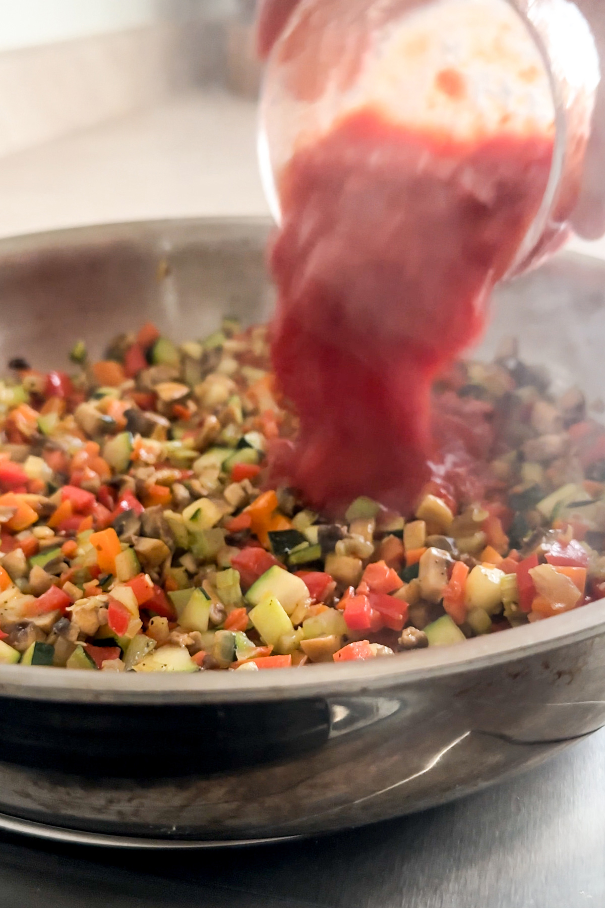 Tomato sauce being poured into a pan with mixed vegetables