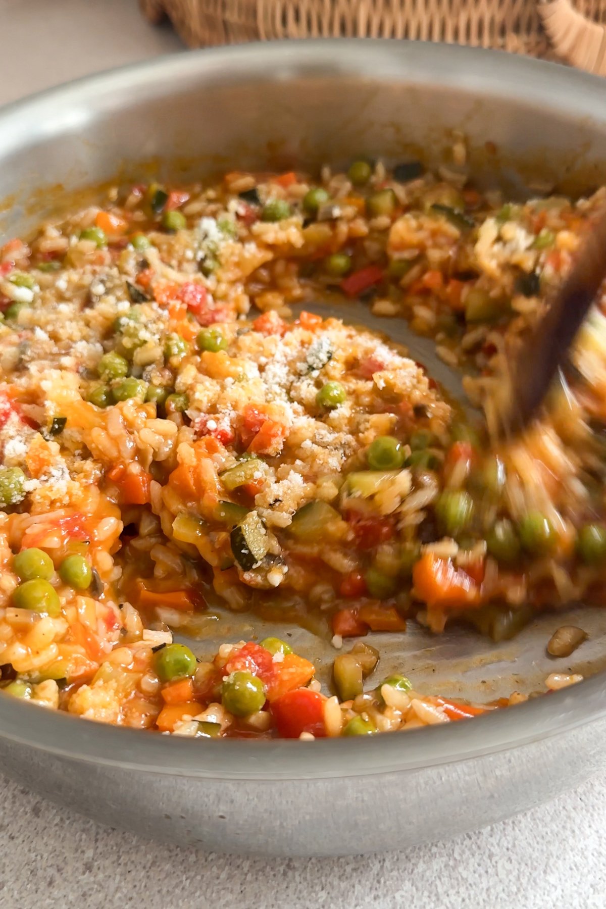 Vegetable risotto in a pan topped with parmesan being stirred with a wooden spoon