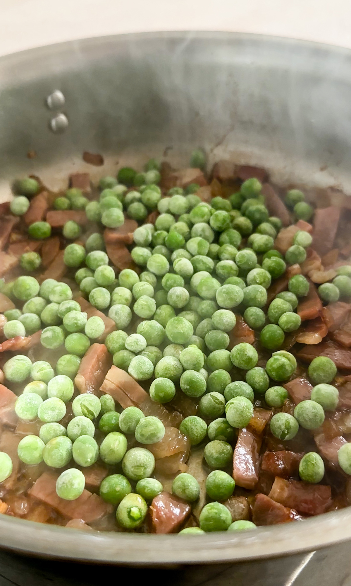 Frozen peas in a pan with sliced prosciutto and onions