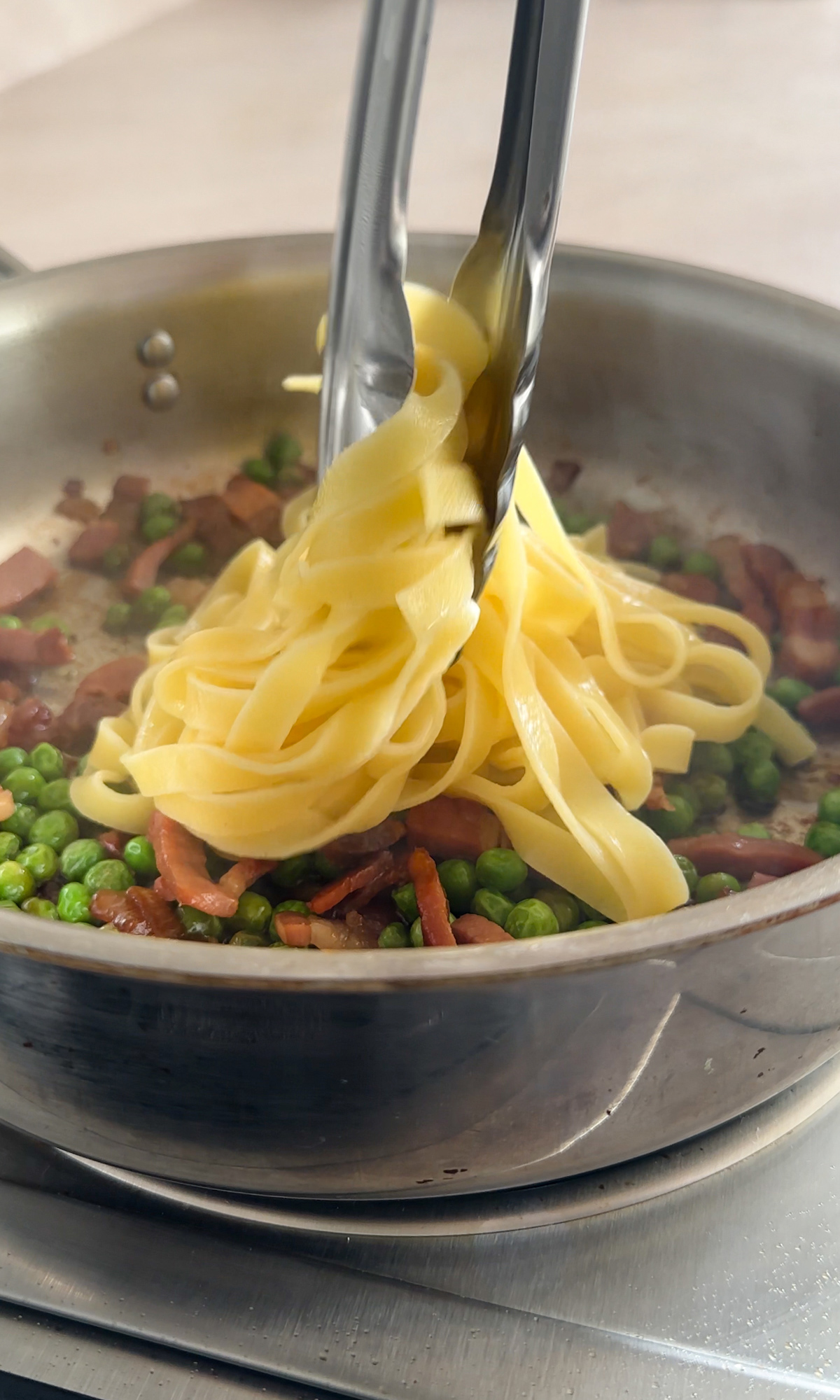 Pasta being placed into a pan with prosciutto and peas