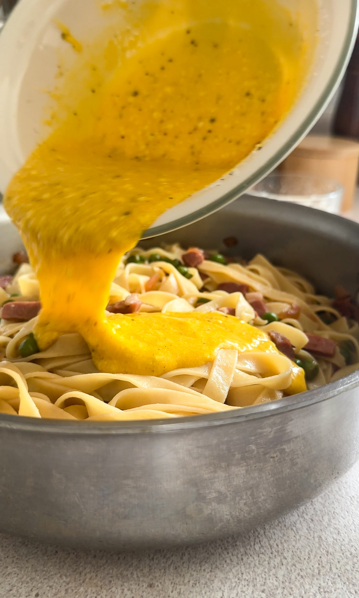 Egg mixture being poured into pan with pasta, prosciutto and peas