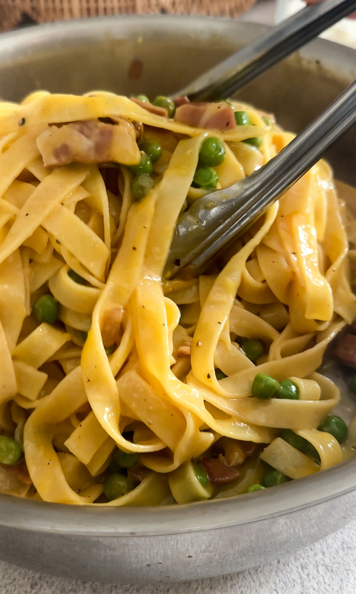 Fettuccine pasta with prosciutto and peas in a pan being mixed with tongs