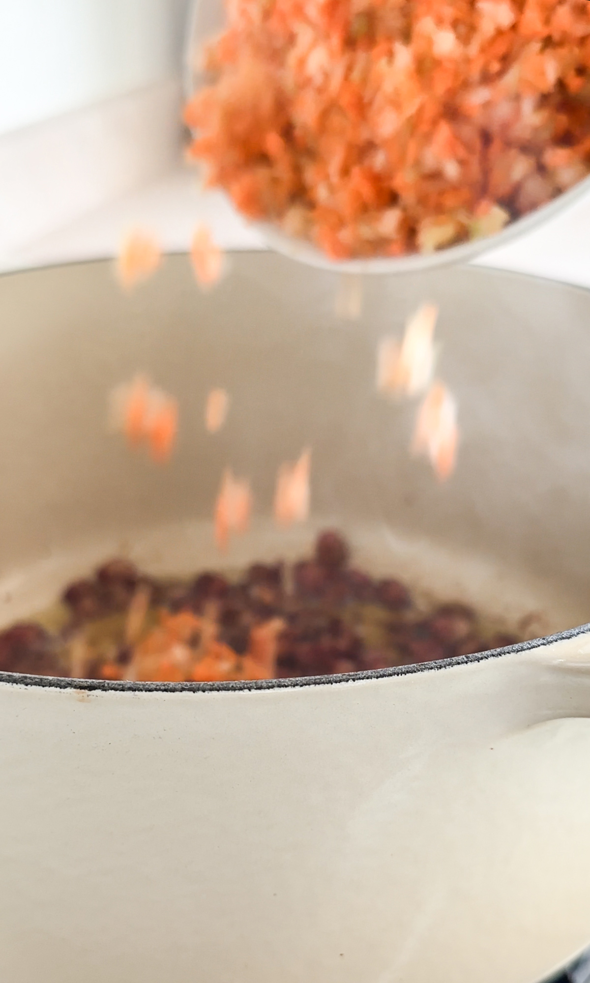 Carrot, celery and onion being placed into a pot with pancetta in it