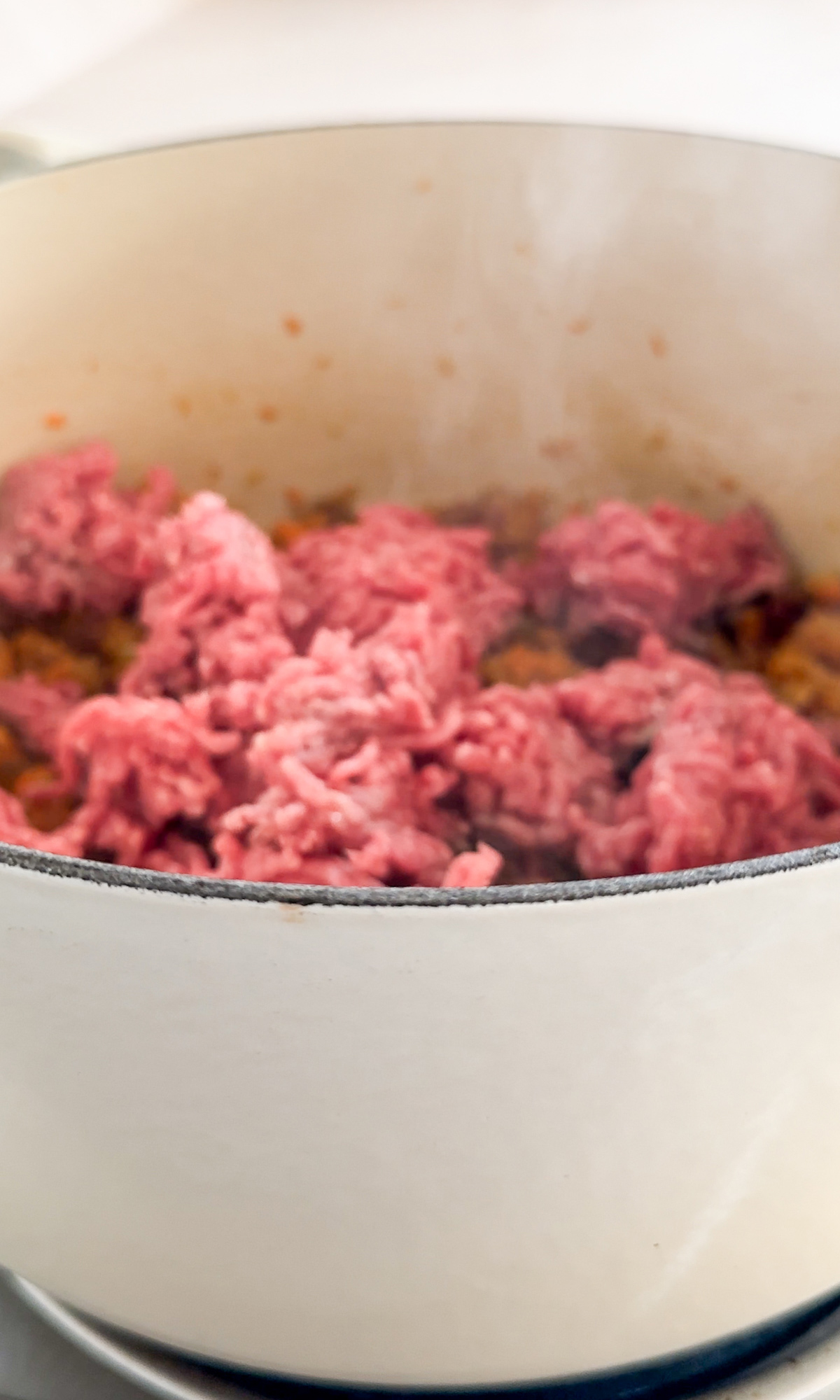 Raw ground beef in a pot on top of soffritto and pancetta