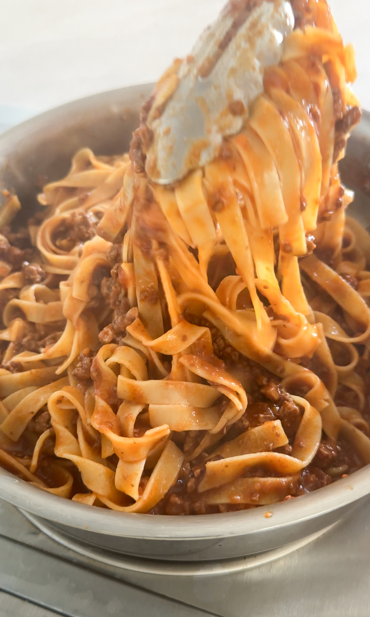 Bolognese pasta being mixed with tongs in a pan