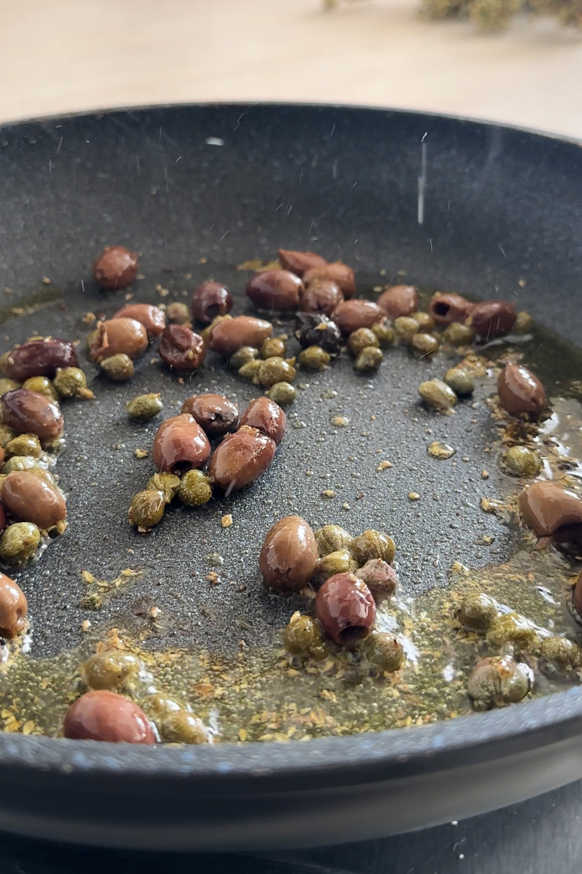 Hot pan with olive oil, dried oregano, capers and olives