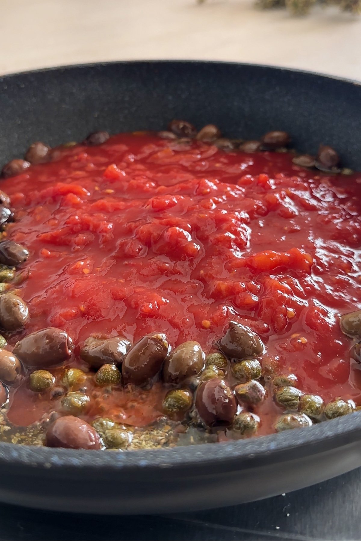 Canned tomatoes, olives and capers in a pan