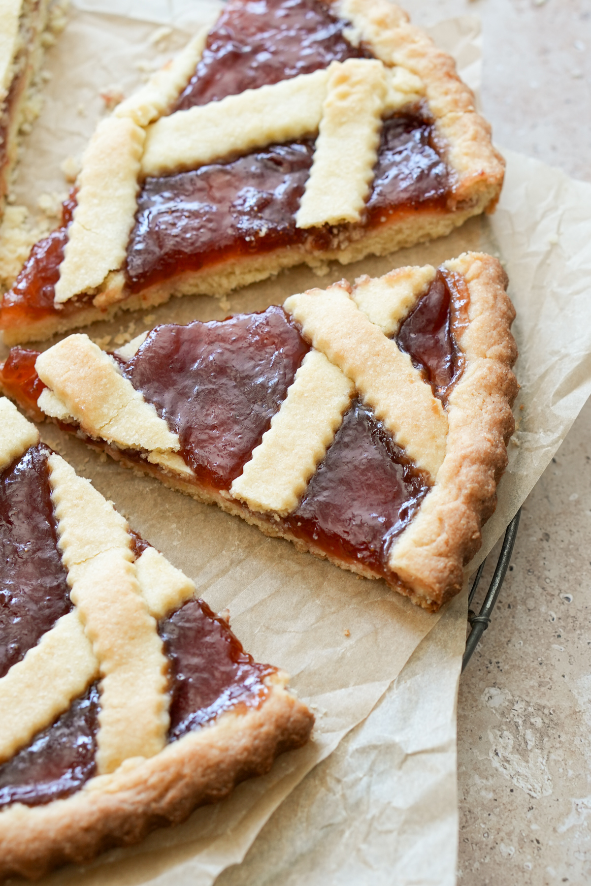 Can't get a more classic Italian dessert than this one - strawberry jam crostata, the flavors are amazing! #crostata #jamcrostata #italiandesserts #italianfood #pinacooks Two slices of crostata cut on parchment paper