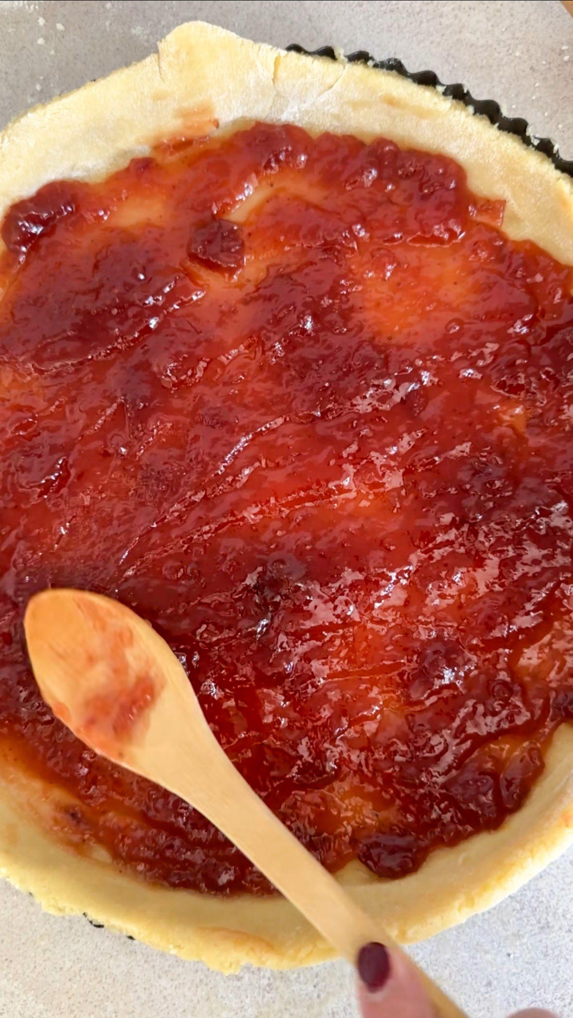 Crostata dough in tart pan with strawberry jam being spread on