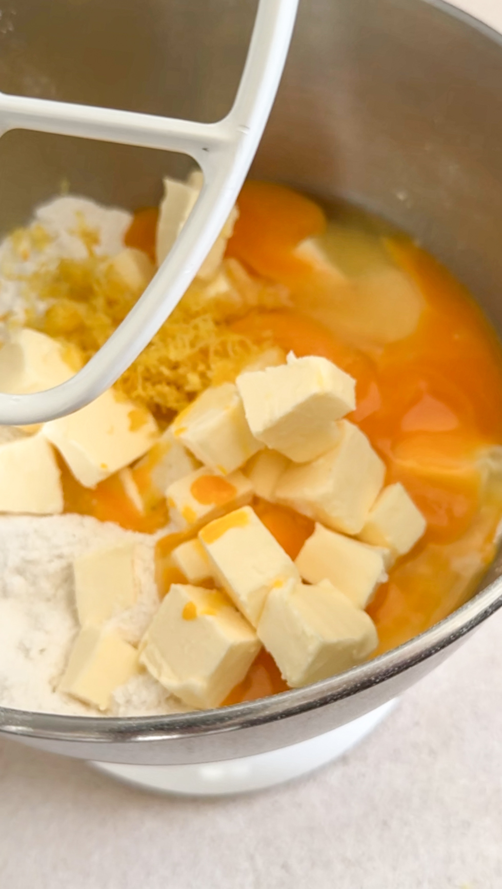Crostata dough ingredients in stand mixer bowl. Cubed butter, flour, baking powder, lemon zest, and eggs
