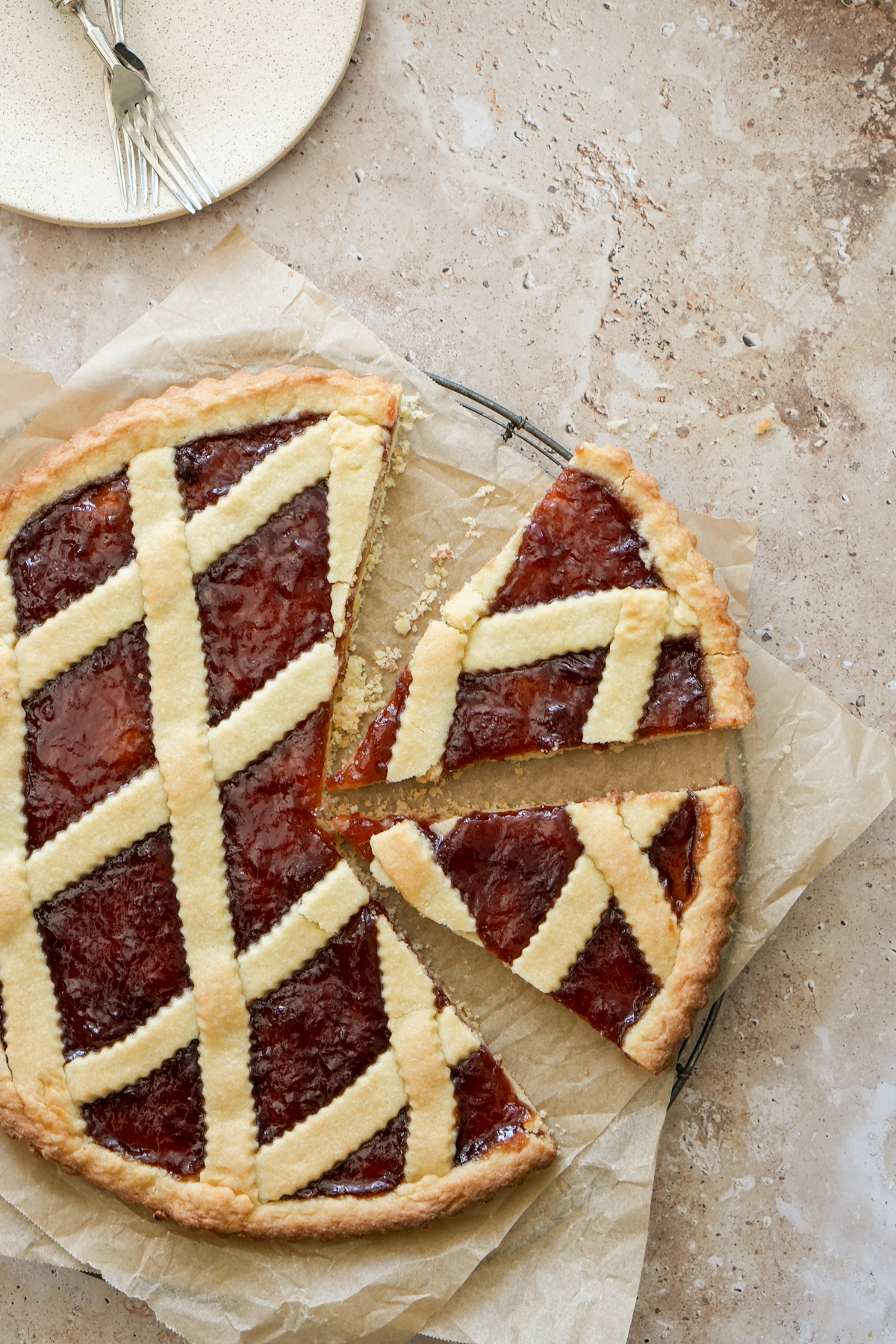 Rustic Italian Jam Crostata. One of the most classic Italian desserts- you'll find it everywhere in Italy! #crostata #jamcrostata #italiandesserts #italianfood #pinacooks Whole jam crostata on a cooling rack with parchment paper, with two slices cut