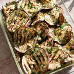 Grilled eggplant rounds in a dish topped with minced garlic and fresh minced parsley