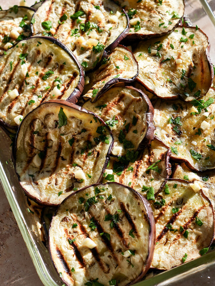 Grilled eggplant rounds in a dish topped with minced garlic and fresh minced parsley